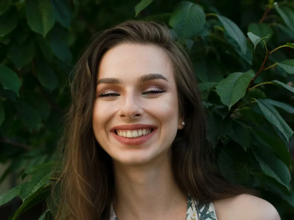 Woman smiling outdoors against green foliage